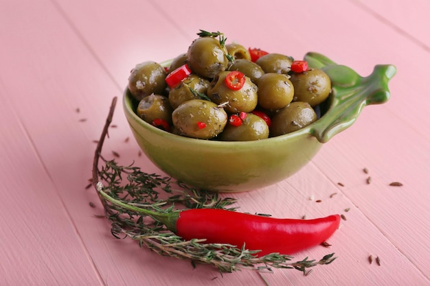 Groene olijven in olie met kruiden en rozemarijn in kom op houten tafel