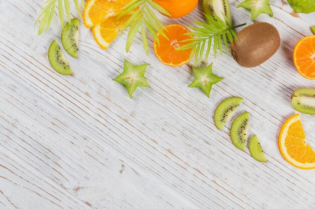 Groene palmbladeren en verse tropische plakjes fruit op witte houten tafel