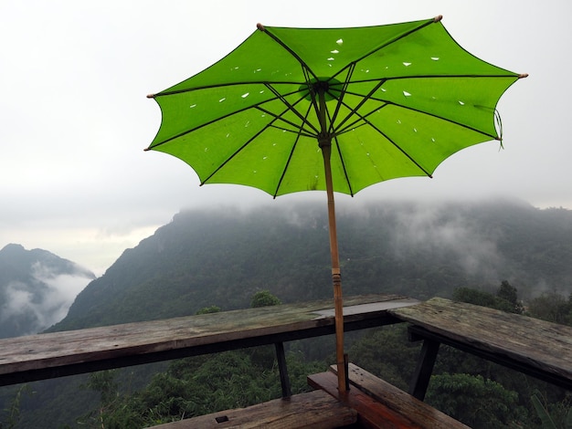 Groene paraplu op houten stoel bij gezichtspunt met regenwolkmist bij pha hi-dorp chiang rai thailand