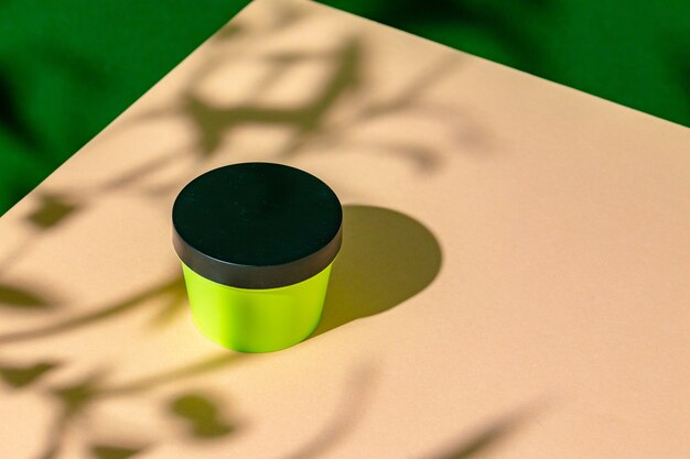 Groene plastic huidverzorgingsproductpot op beige oppervlak met schaduw erop
