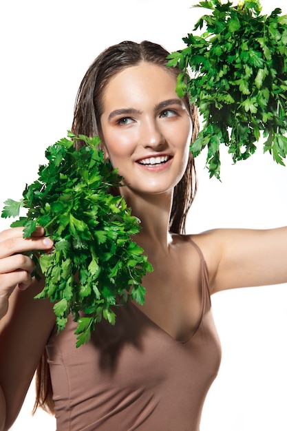 Groene plons. Close up van mooie jonge vrouw met peterselie op witte achtergrond. Concept van cosmetica, make-up, natuurlijke en eco-behandeling, huidverzorging. Glanzende en gezonde huid, mode, gezondheidszorg.