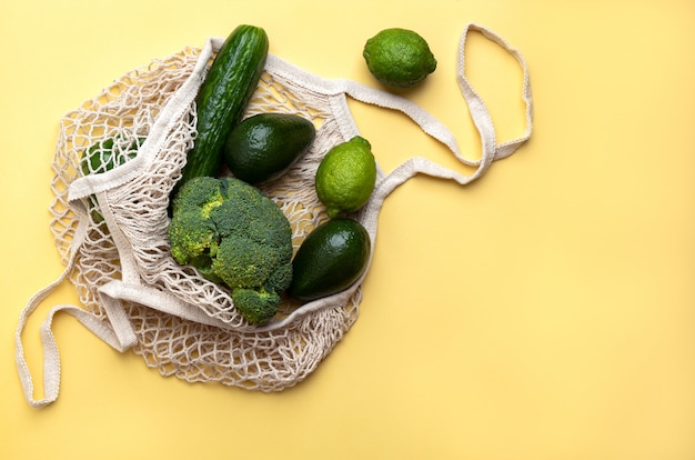 Groene producten in een herbruikbare zak op een gele achtergrond