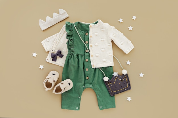 Groene romper met gebreide trui, kinderhandtas, katoenen kroontje en babylaarsjes. Set babykleding en accessoires. Mode kinderoutfit. Platliggend, bovenaanzicht