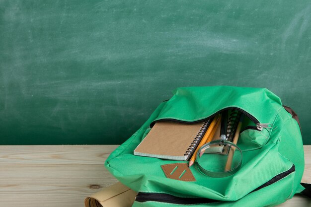 Groene rugzaknotitieboekjes en schoolspullen op de achtergrond van het bord