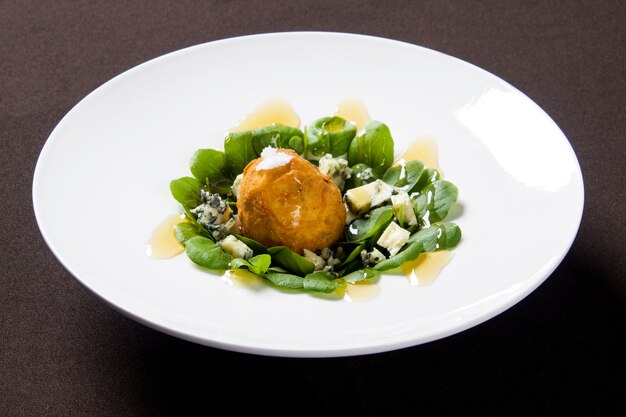 Groene salade met gebakken ei en kaas op een witte plaat.