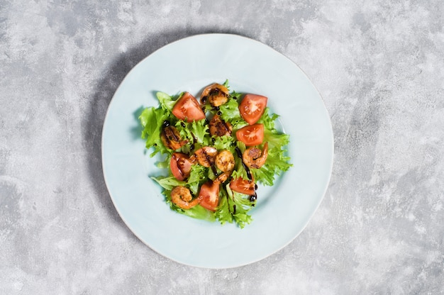 Groene salade met gegrilde garnalen op grijs.