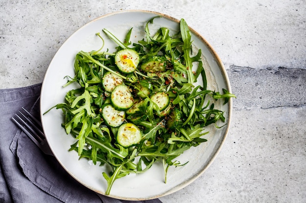 Groene salade van rucola en komkommers met olie en kruiden in een grote grijze schaal.