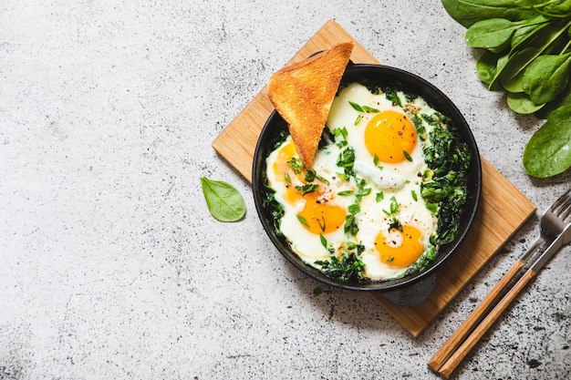 Groene shakshuka in een gietijzeren koekenpan gebakken eieren met spinazie en gebakken toast gezond voedzaam ontbijt