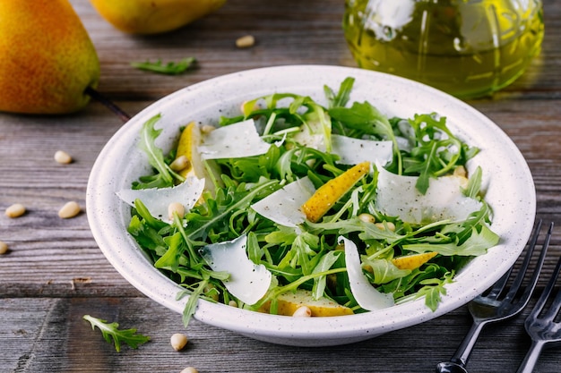 Groene slakom rucola met peren, Parmezaanse kaas en pijnboompitten op een houten ondergrond