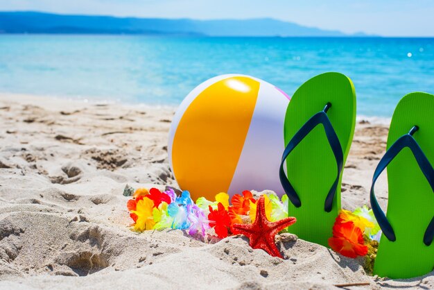 Groene slippers en strandbal op het zand