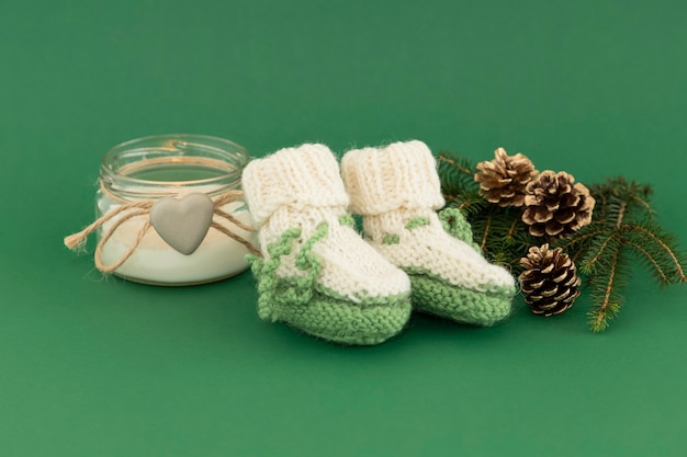 Groene slofjes voor een pasgeborene op Kerstmis met kaarsen en een dennentak.