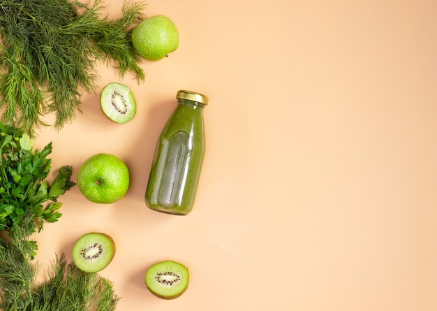 Groene smoothie in een transparante fles op een beige achtergrond. De gesneden groenten en fruit liggen klaar. Gezond eten, plat gelegd. Kopieerruimte.