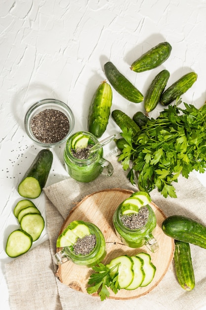 Groene smoothie met komkommer in een glazen pot. Verse rijpe groenten, Groenen, en chiazaden. Trendy hard licht, donkere schaduw. Witte stopverfachtergrond, bovenaanzicht