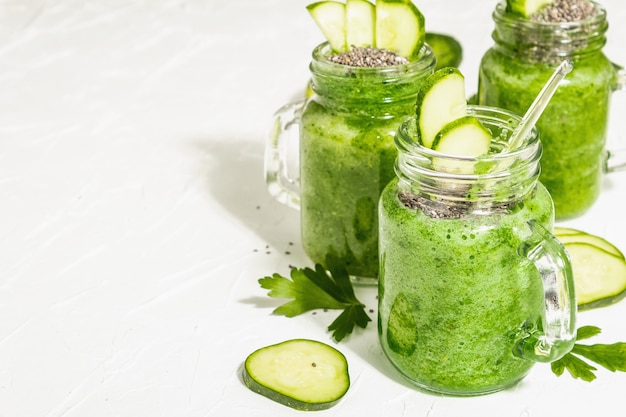 Groene smoothie met komkommer in een glazen pot. Verse rijpe groenten, Groenen, en chiazaden. Trendy hard licht, donkere schaduw. Witte stopverfachtergrond, kopieer ruimte