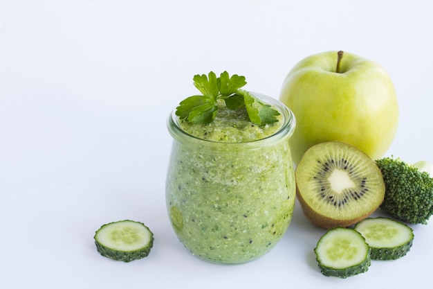 Groene smoothie of puree in de kleine glazen pot op de witte achtergrond. Detailopname. Ruimte kopiëren.