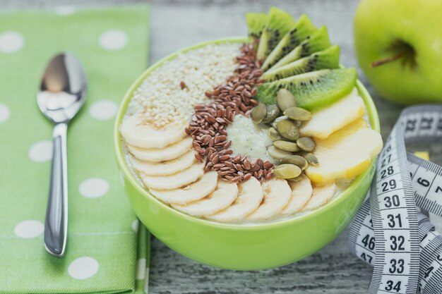 Groene smoothiekom gegarneerd met kiwi, banaan, appels en zaden op witte rustieke houten achtergrond voor gezond veganistisch vegetarisch dieetontbijt. gezond voedselconcept. bovenaanzicht