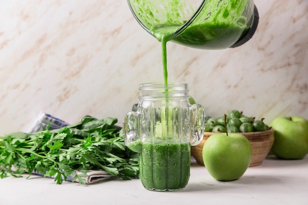 Groene smoothies worden uit een glazen mengkom in een glas gegoten