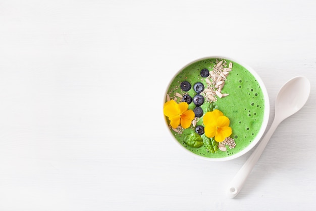 Groene spinazie smoothie kom met bosbessen, chiazaad en eetbare viooltje bloemen