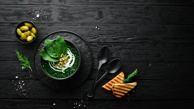 Groene Spinazieroomsoep met room en pompoenpitten in een zwarte kom Gezonde voeding Bovenaanzicht Rustieke stijl