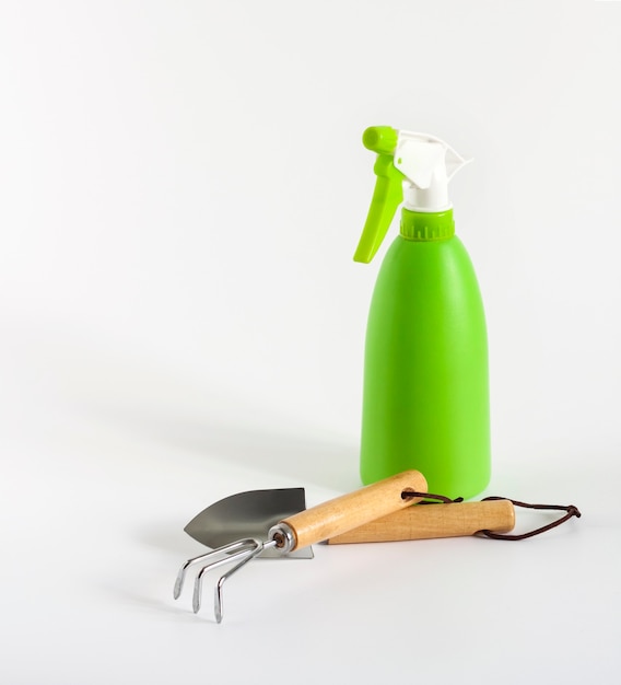 Groene spuitfles en kleine tuingereedschap op witte achtergrond met kopieerruimte. Tuinieren en plantenverzorging