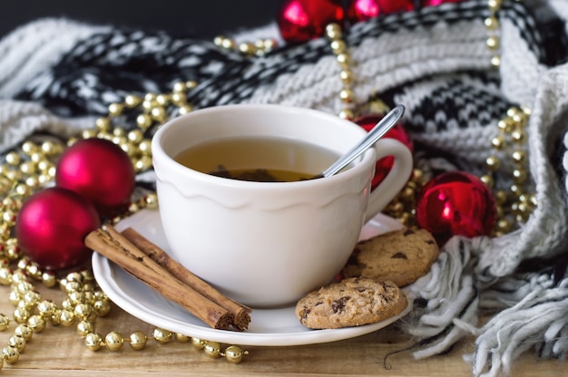 Groene thee in een witte kop met kaneelstokjes, chocoladekoekjes, gebreide deken en kerstdecor