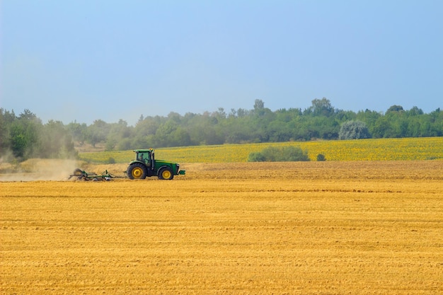 Groene tractor met eg die in de herfst op het gele veld werkt