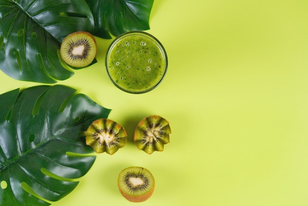 Groene vegetarische smoothie op een groene achtergrond met de kiwihelften en tropische bladeren, schoon voedselconcept, hoogste mening, exemplaar van ruimte