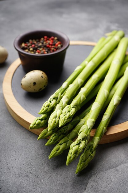 Groene verse asperges en keukenbord op grijs oppervlak, close-up. verticaal