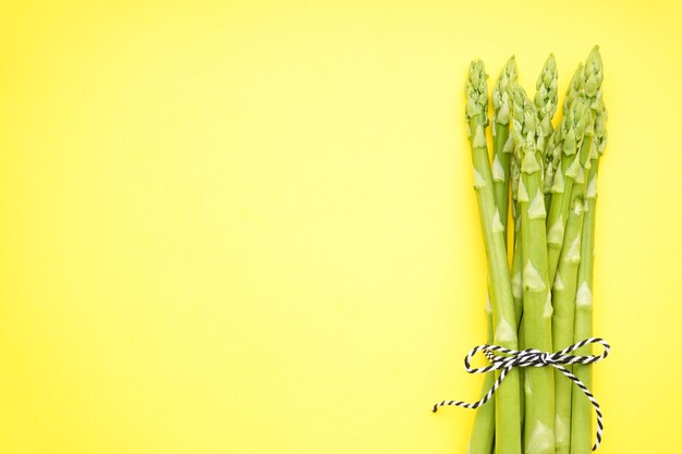 Groene verse asperges op een gele ondergrond, ruimte voor tekst. Bovenaanzicht.