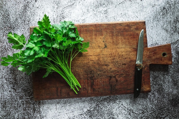 Groene verse geurige peterselie met een mes voor het snijden van greens ligt op een houten bord op een grijze achtergrond 2