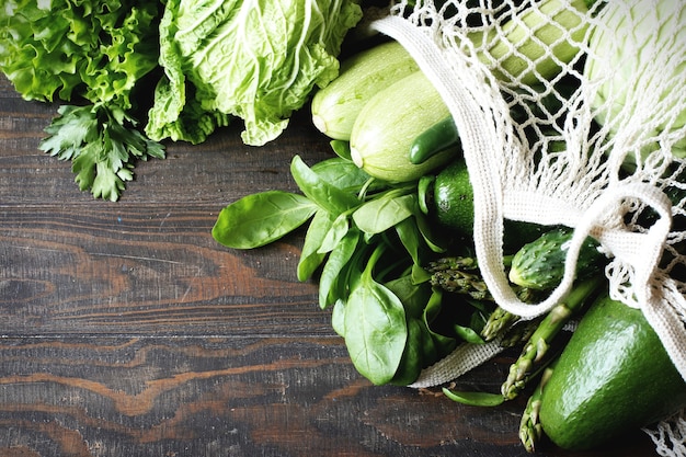 Foto groene verse groenten, avocado, broccoli, spinazie, komkommers in een bovenaanzicht van een netzak.