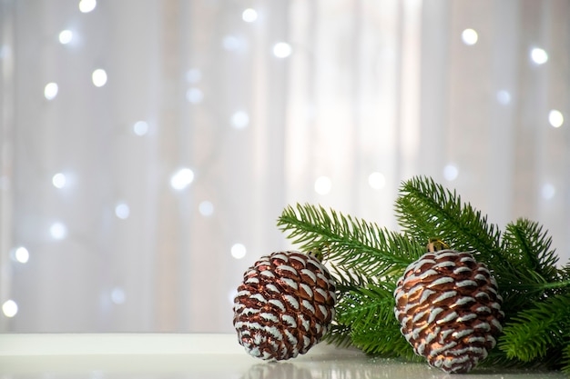 Groene vuren takken en dennenappels op achtergrond van witte bokeh lichten met tulle venster