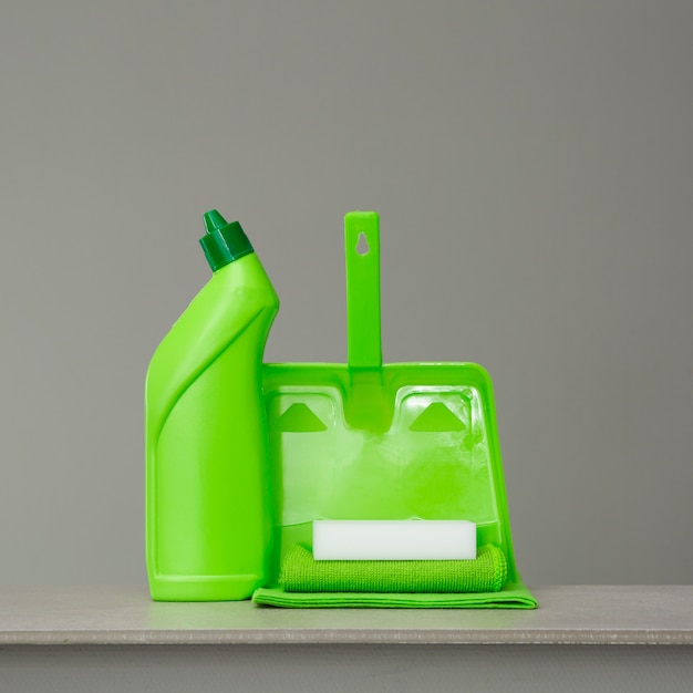 Groene wasmiddelfles voor toilet, spons, schep en stofdoek op grijs.