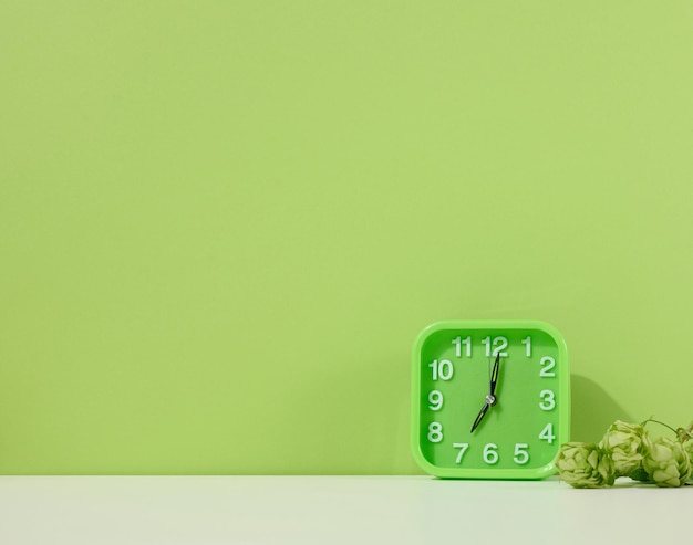 Groene wekker staat op een witte tafel groene achtergrond Terug naar school