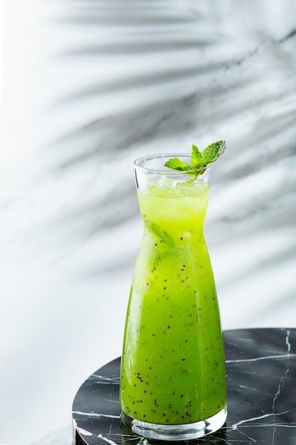 Groene zomerlimonade in kruik op lichte achtergrond met schaduw van tropische plant. Limonade met kiwi en ijs