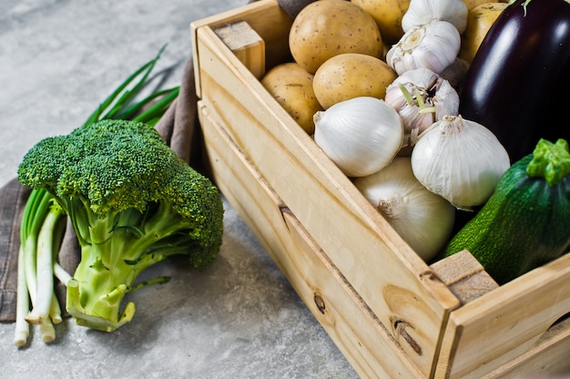 Groenten in een houten kist: aardappelen, uien, knoflook, aubergine, courgette, broccoli, groene uien.