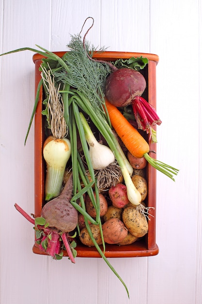 Groenten in een mand: bieten, uien, knoflook, dille, aardappelen, wortelen op een oude houten achtergrond