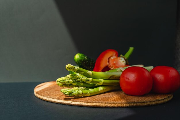 Groenten liggen op een houten plank tomaten asperges komkommers rode paprika's bruin donkergrijze achtergrond plaats voor tekst