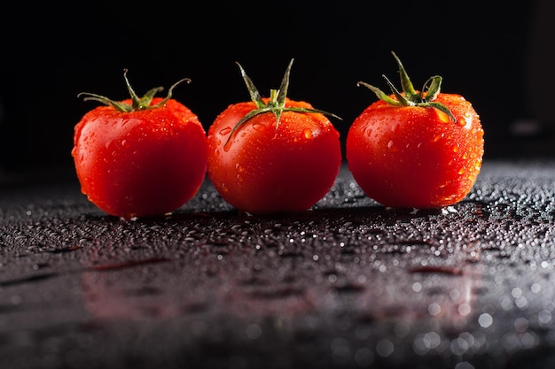 Groenten op een donkere achtergrond Drie verse tomaten