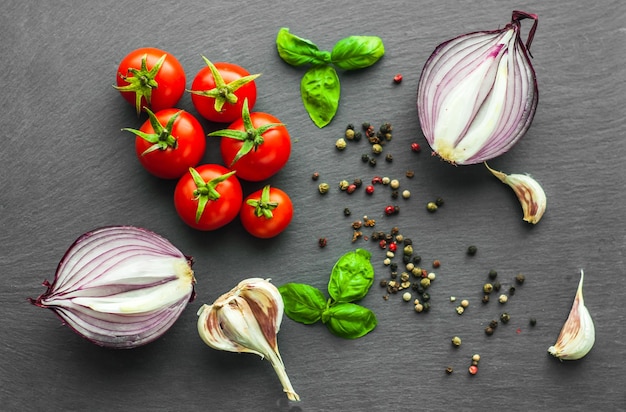 groenten op een zwarte getextureerde kleur, bovenaanzicht, sappige tomaten, uien, basilicum, peperkorrels, knoflook