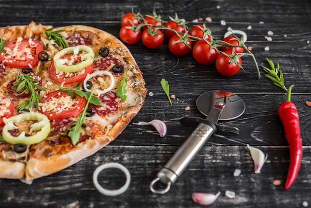 Groenten, paddestoelen en tomatenpizza op een zwarte houten achtergrond.