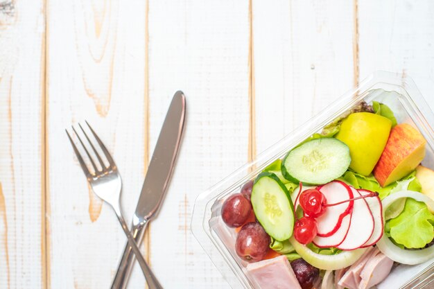 Groentensalade in plastic kom op witte houten lijst