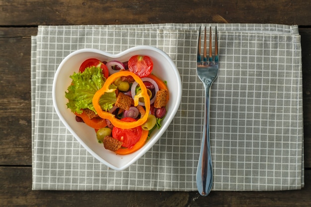 Groentesalade in een hartvormige plaat op een houten tafel op een servet.