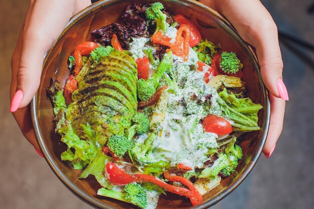 Foto groentesalade met avocado, komkommer, kersen, tomaten, chard en broccoli op een bord op de houten tafel