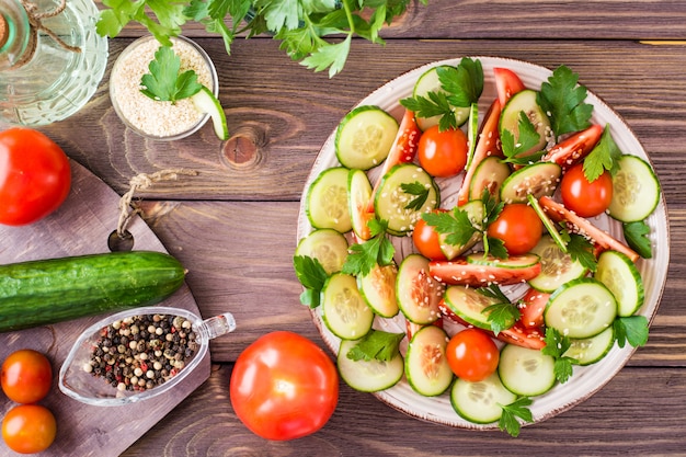 Groentesalade van verse komkommers, tomaten, peterselie en sesamzaadjes op een bord op een houten tafel.