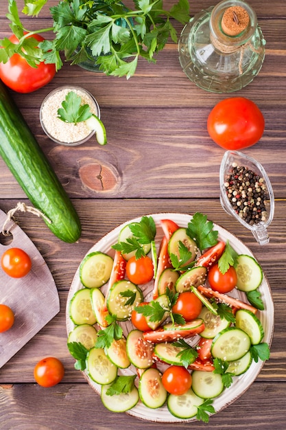 Groentesalade van verse komkommers, tomaten, peterselie en sesamzaadjes op een bord op een houten tafel.