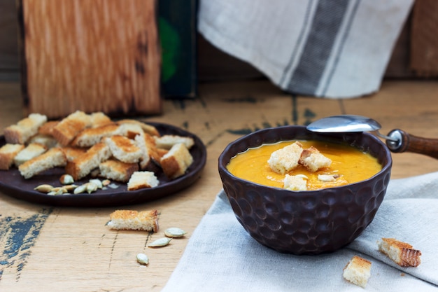 Groentesoeppuree van pompoen, wortelen en selderij, geserveerd met croutons en pompoenpitten. rustieke stijl.