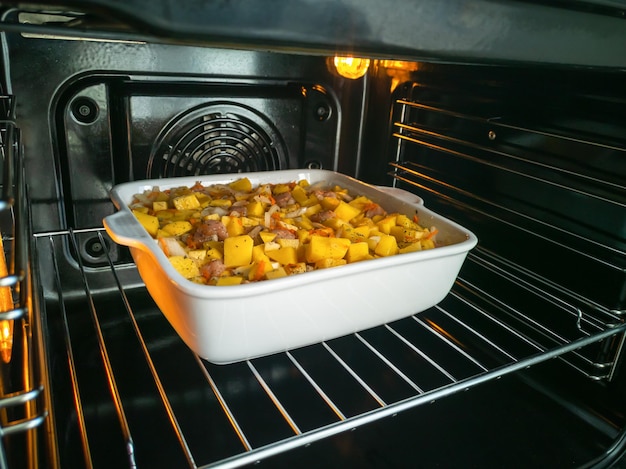 Groentestoofpot met aardappelen, vlees en kruiden in een witte keramische ovenschaal