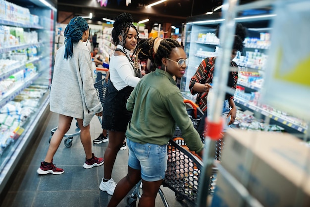 Groep afrikaanse dames met winkelwagentjes in de buurt van koelkastplank die zuivelproducten verkopen die zijn gemaakt van melk in de supermarkt