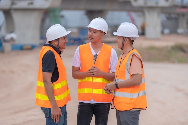 Groep Aziatische ingenieurs bespreken het werk op de bouwplaats in aanbouw Het aannemersteam bespreekt het ontwerp van de constructie Drie arbeiders werken buiten